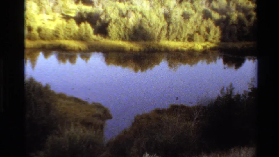 Western USA 1980 home-movie frame of a calm river or pond with vegetation mirrored across the water surface.