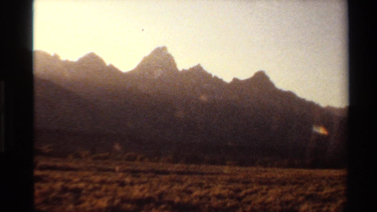 Mountain silhouette and dry open foreground with warm sky and lens flare.