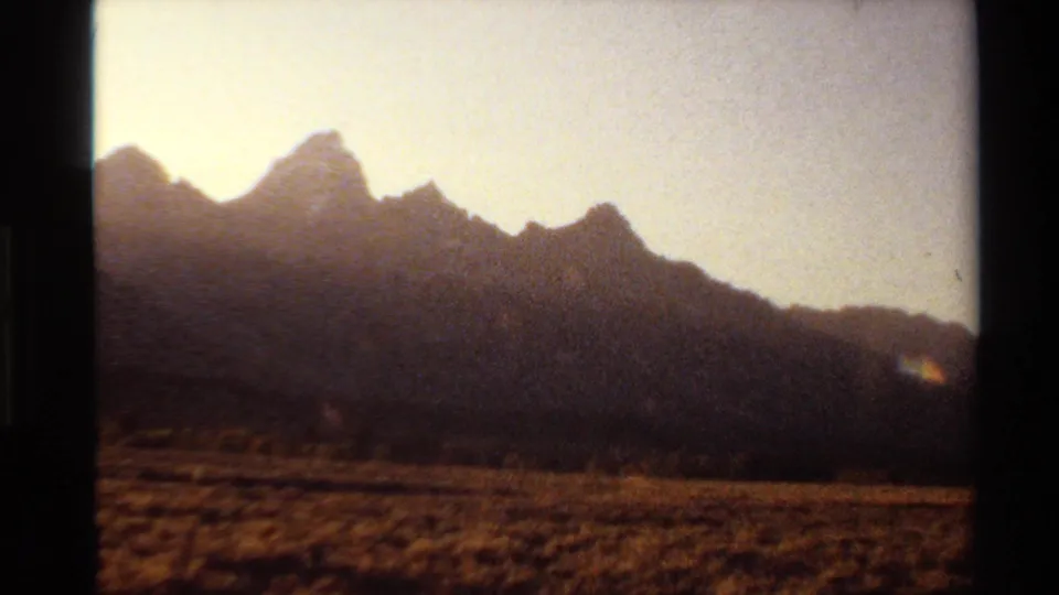 1980 Western USA 8mm frame showing distant mountain peaks over dry grassland, softened by haze and warm exposure.