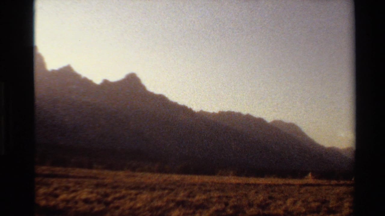 1980 8mm Western U.S. home-movie frame of dark mountain ridges, dry grassland, and warm evening sky.