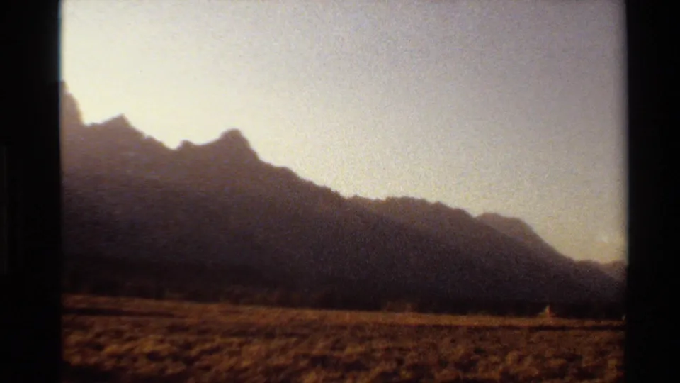 1980 8mm Western U.S. home-movie frame of dark mountain ridges, dry grassland, and warm evening sky.