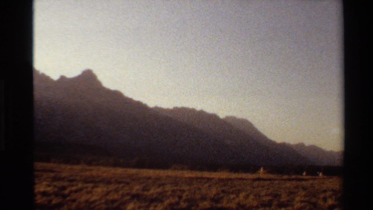 Western U.S. 8mm frame showing silhouetted mountains, dry grassland, and small distant people in sunset light.