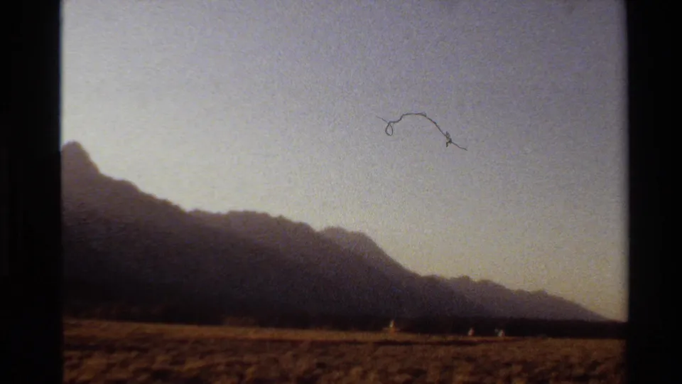 8mm Western U.S. sunset landscape with silhouetted mountains, dry foreground, and small distant people.