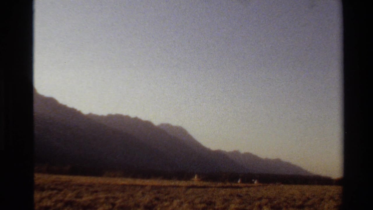 1980 Western U.S. 8mm frame showing a silhouetted mountain range across dry open ground beneath a fading sky.