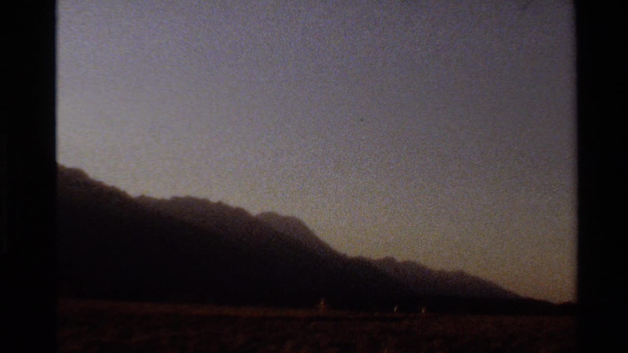 Grainy 8mm view of a dark mountain range and arid foreground, likely filmed in the Western United States in 1980.