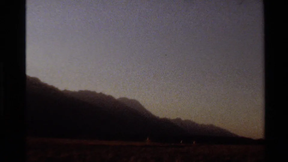 Grainy 8mm view of a dark mountain range and arid foreground, likely filmed in the Western United States in 1980.