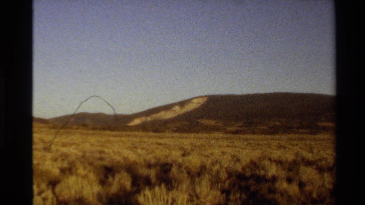 Arid scrub field and distant ridge appear within the 8mm frame edges.