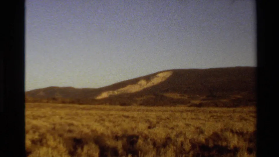Western U.S. 8mm landscape frame with a wide sagebrush plain, distant ridge, and clear sky in warm faded color.