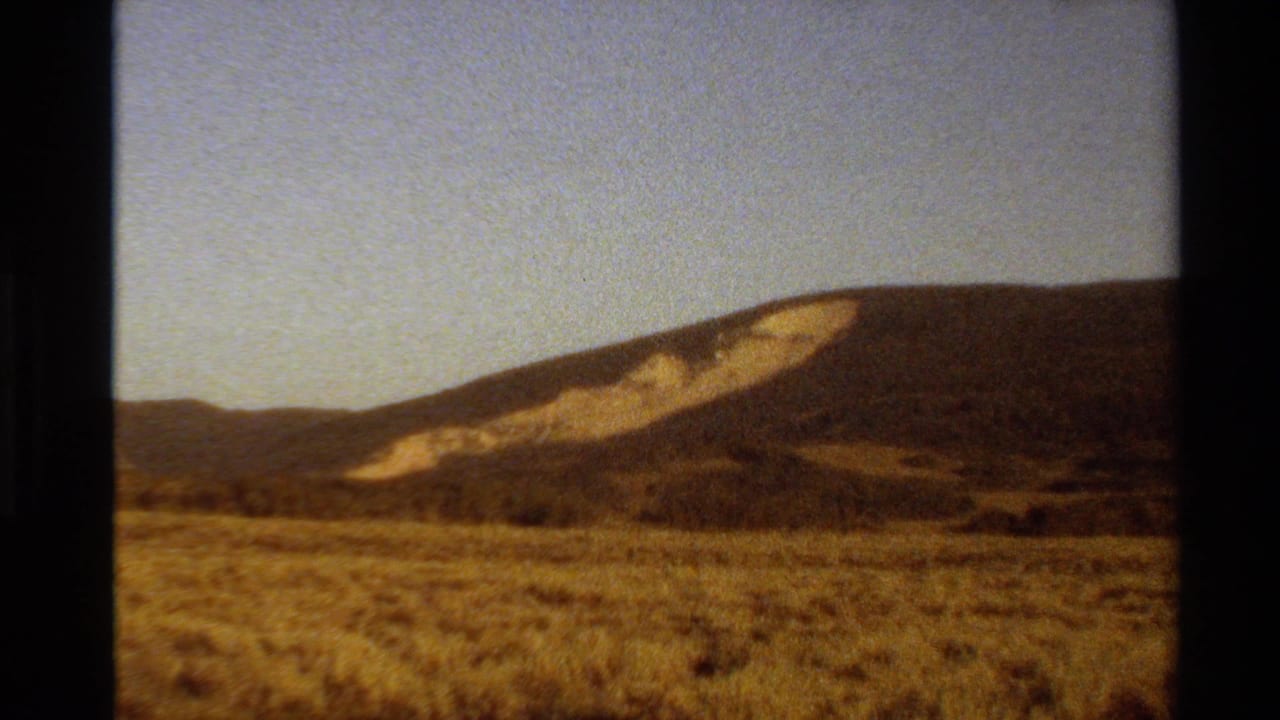 Wide field and rounded hill with a light patch of exposed earth on the slope.