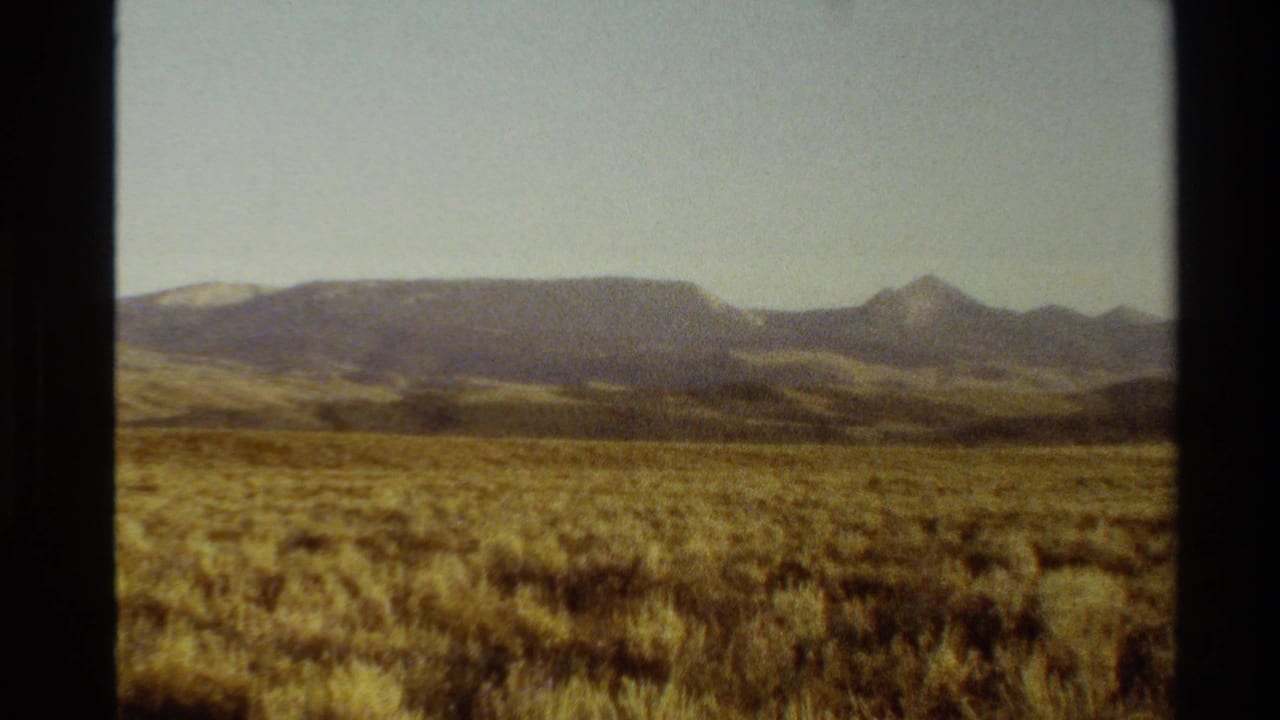 Open dry plain and distant mountain range seen through dark 8mm frame edges.
