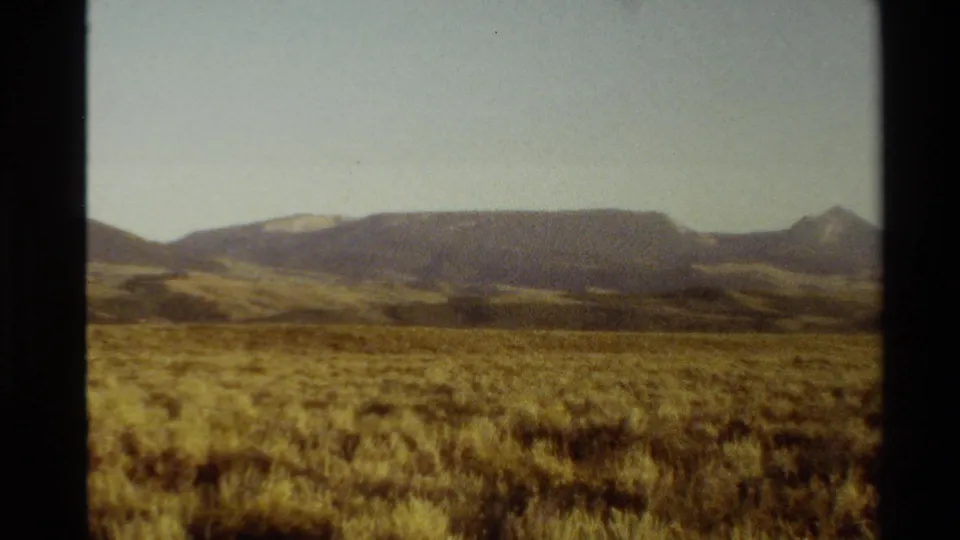 Western USA 1980 home-movie frame showing a dry plain, layered hills, a distant mountain peak, and warm grainy 8mm color.