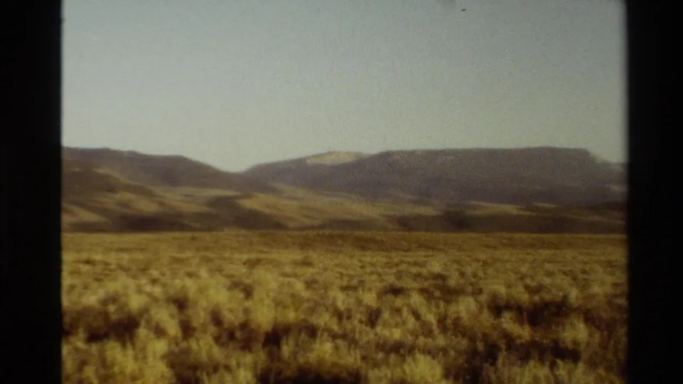 1980 Western USA 8mm frame showing golden-brown grassland, low mountain ridges, a pale sky, and visible film-frame borders.