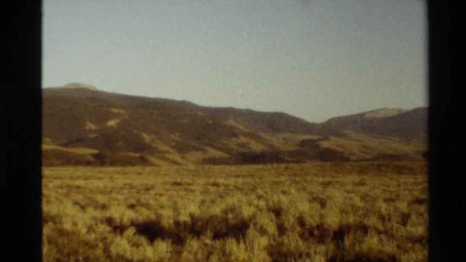 1980 8mm landscape frame showing an open dry meadow and distant mountain ridges in the Western United States.