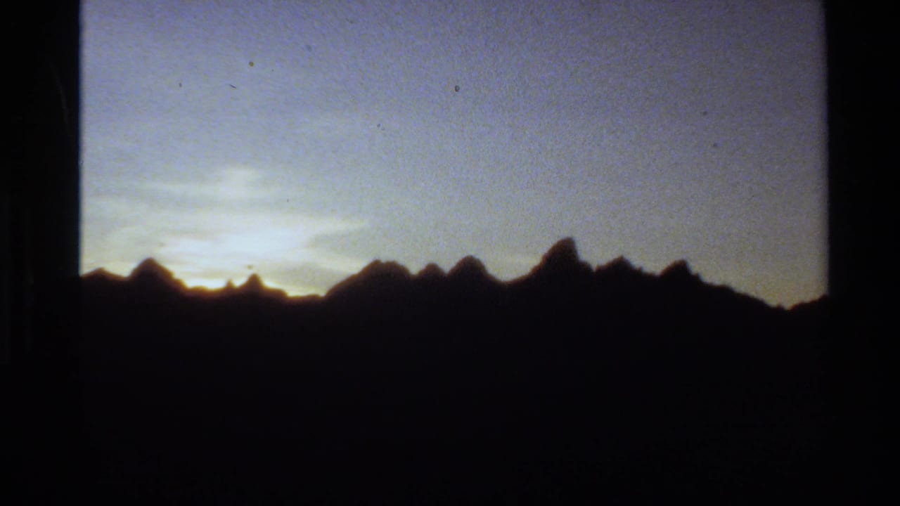1980 Western USA home-movie frame showing mountain peaks in silhouette beneath a fading blue and yellow evening sky.