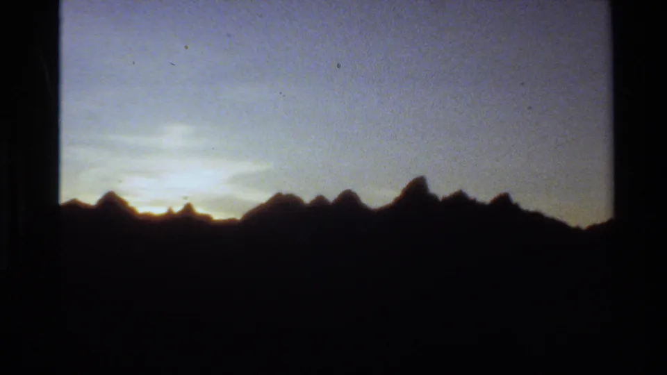 1980 Western USA home-movie frame showing mountain peaks in silhouette beneath a fading blue and yellow evening sky.