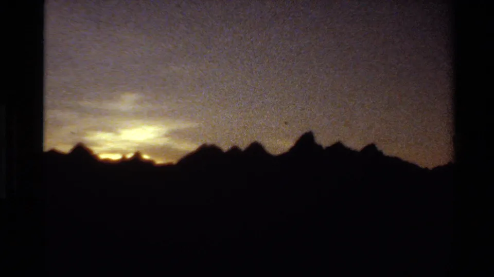 Grainy 8mm frame from the 1980 Western USA clip, with warm fading light behind a shadowed mountain ridge.