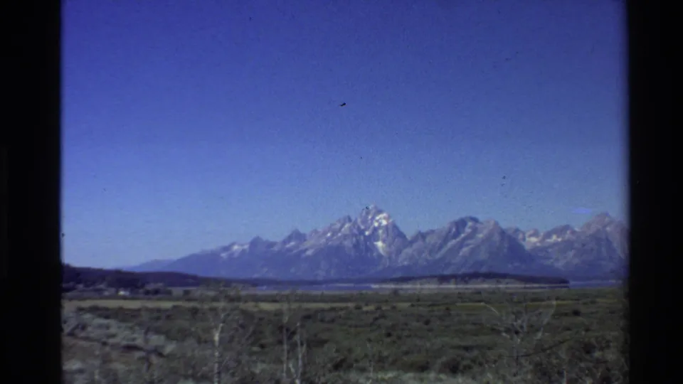 Final 1980s 8mm frame of a broad Western U.S. mountain landscape, with muted grassland foreground and snow-bright peaks in the distance.