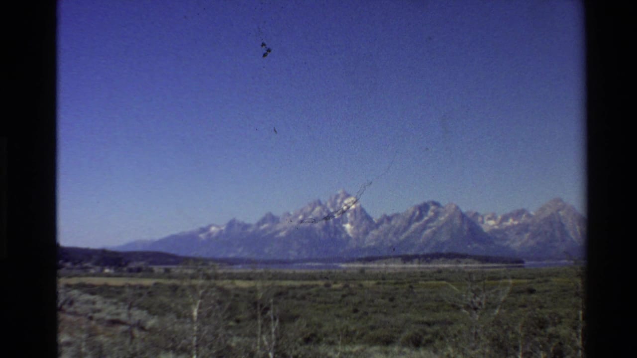 1980 8mm view of snow-capped mountains rising beyond flat grassy lowlands in the Western United States.