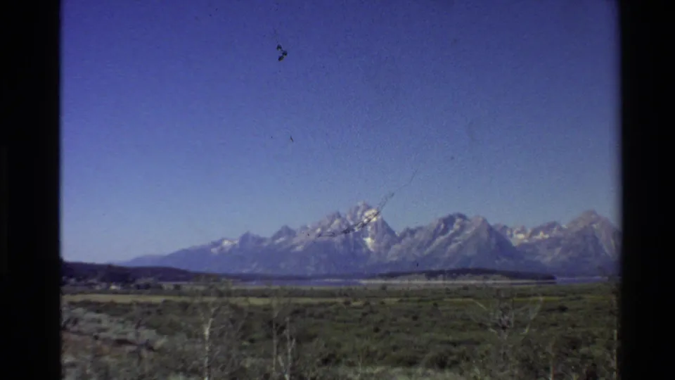 1980 8mm view of snow-capped mountains rising beyond flat grassy lowlands in the Western United States.