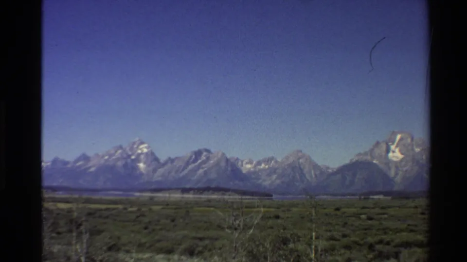 Western USA 8mm travel frame from 1980 showing a broad mountain range, blue sky, and low vegetation in the foreground.