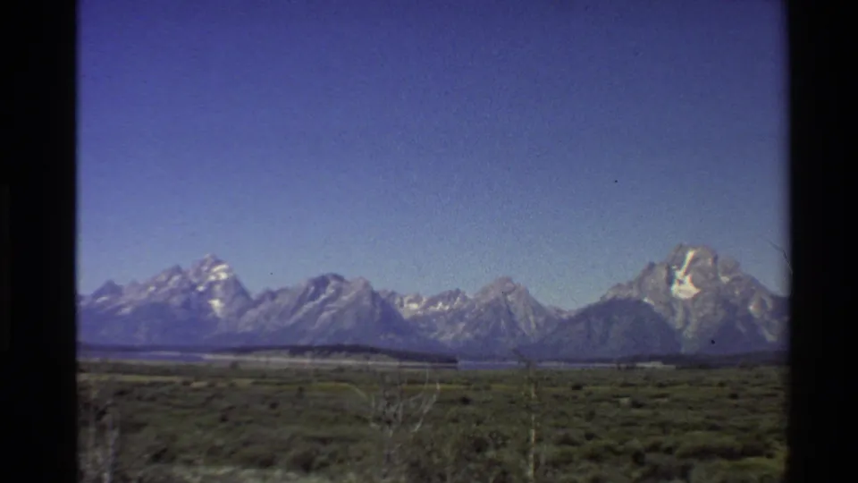 1980 8mm home-movie still of snow-capped peaks beyond scrub-covered open ground in the Western USA.