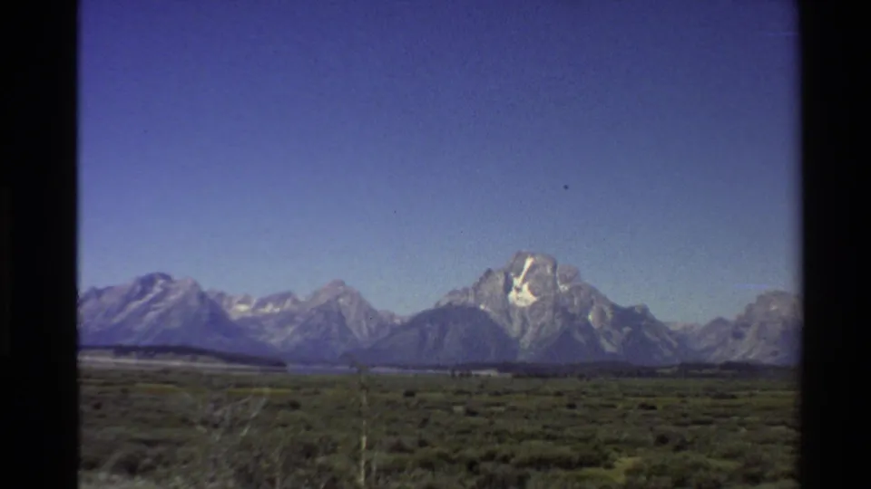 1980 Western U.S. 8mm frame with a prominent Teton peak above open valley vegetation.