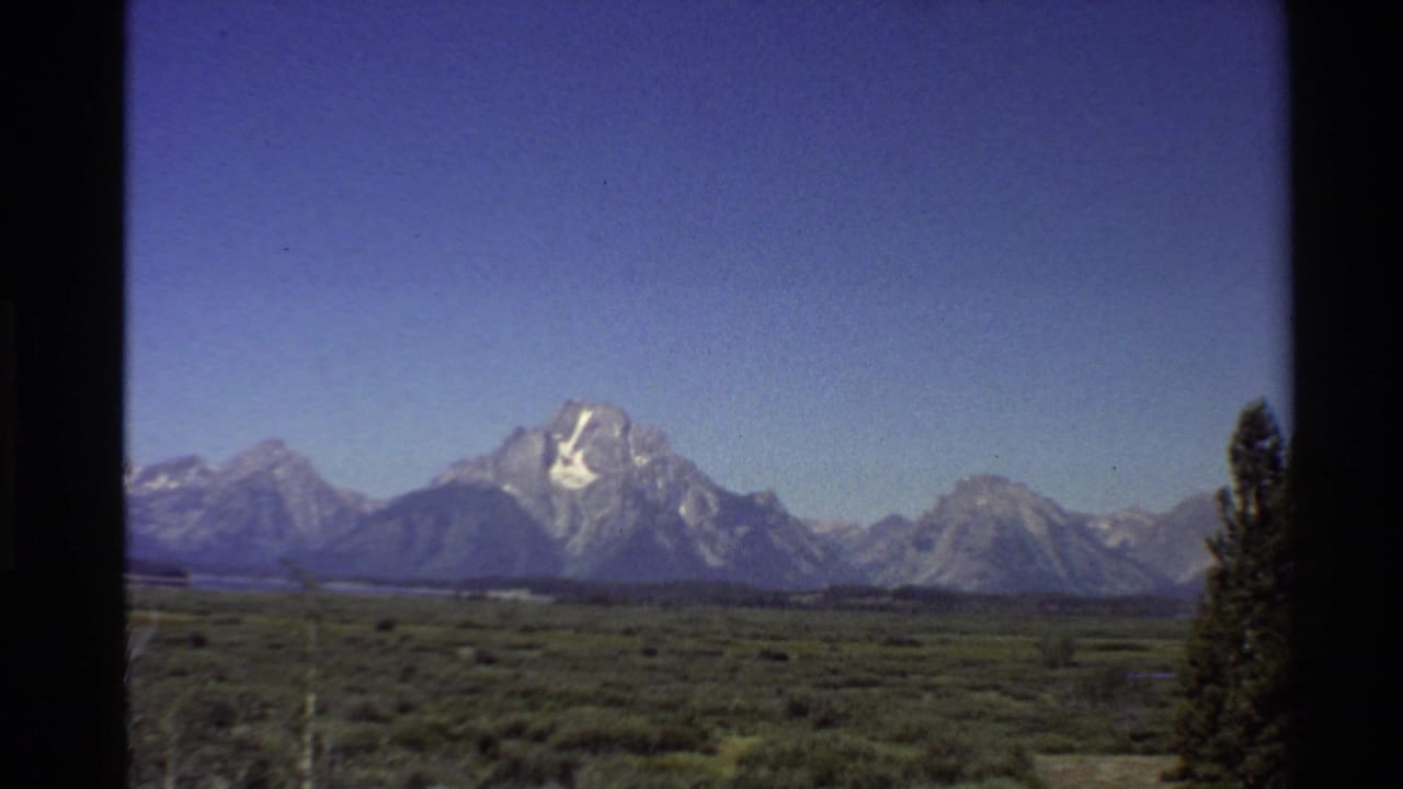 Mountain peaks and valley landscape with a tree at the far right edge.