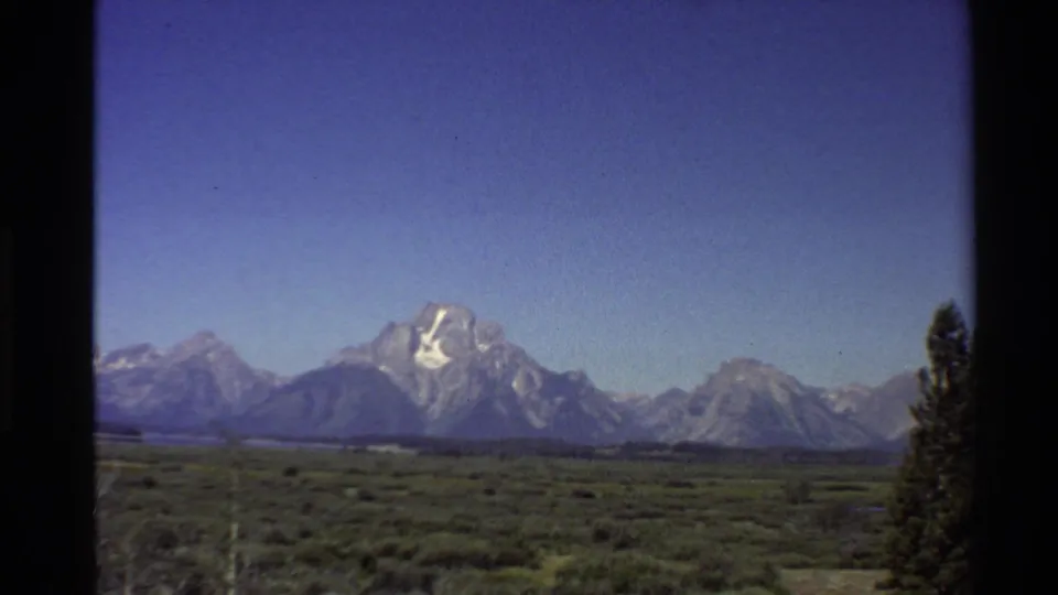 1980 8mm frame showing the Teton Range across a wide valley, with open sky and a dark tree along the right border.