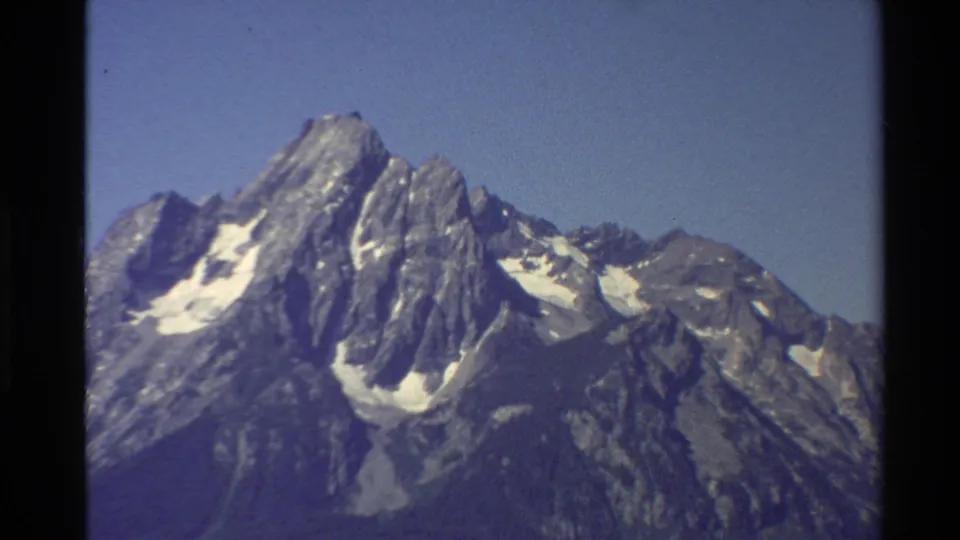 Archival 8mm frame of a rugged Western United States mountain summit with scattered snow and soft home-movie focus.