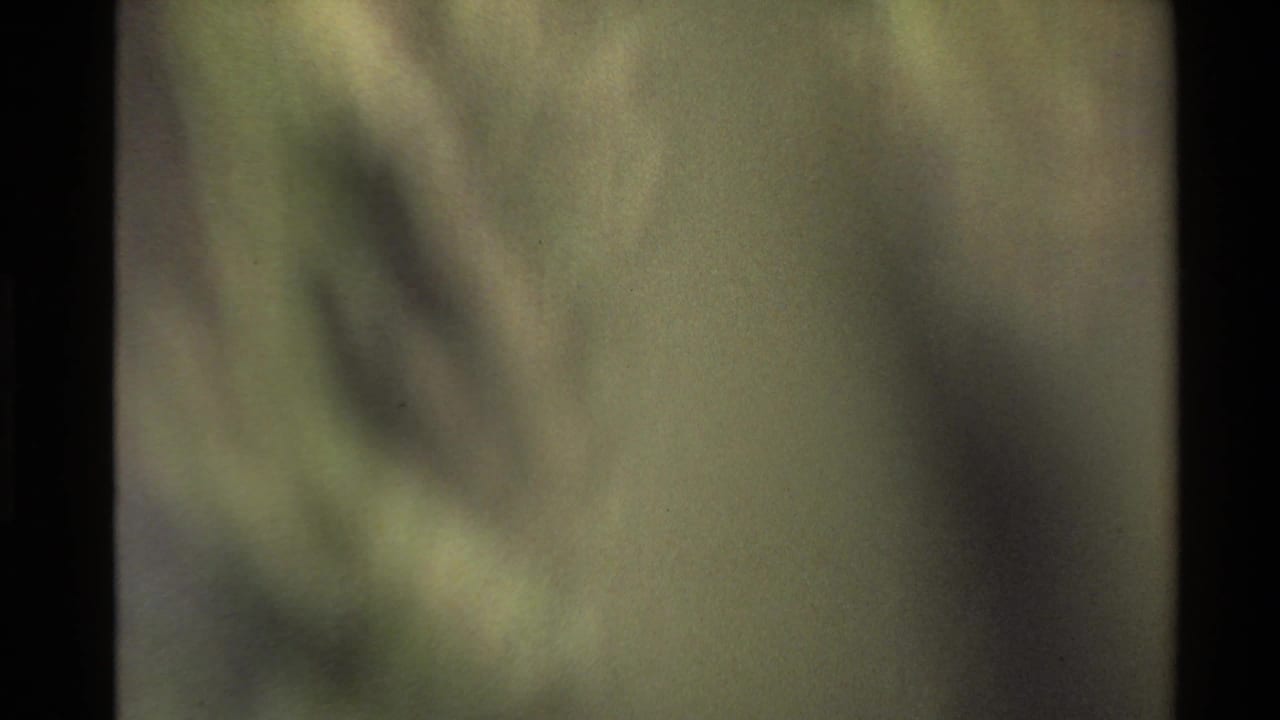 Soft-focus 8mm frame from the Western U.S. clip, showing abstract green-gray shapes as the camera moves away from the clear landscape view.