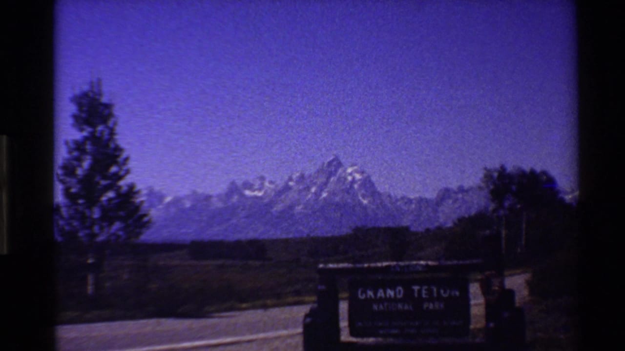 1980 8mm frame appears to show the Grand Teton National Park entrance sign beside a road, with the Teton range in the background and a strong purple cast.