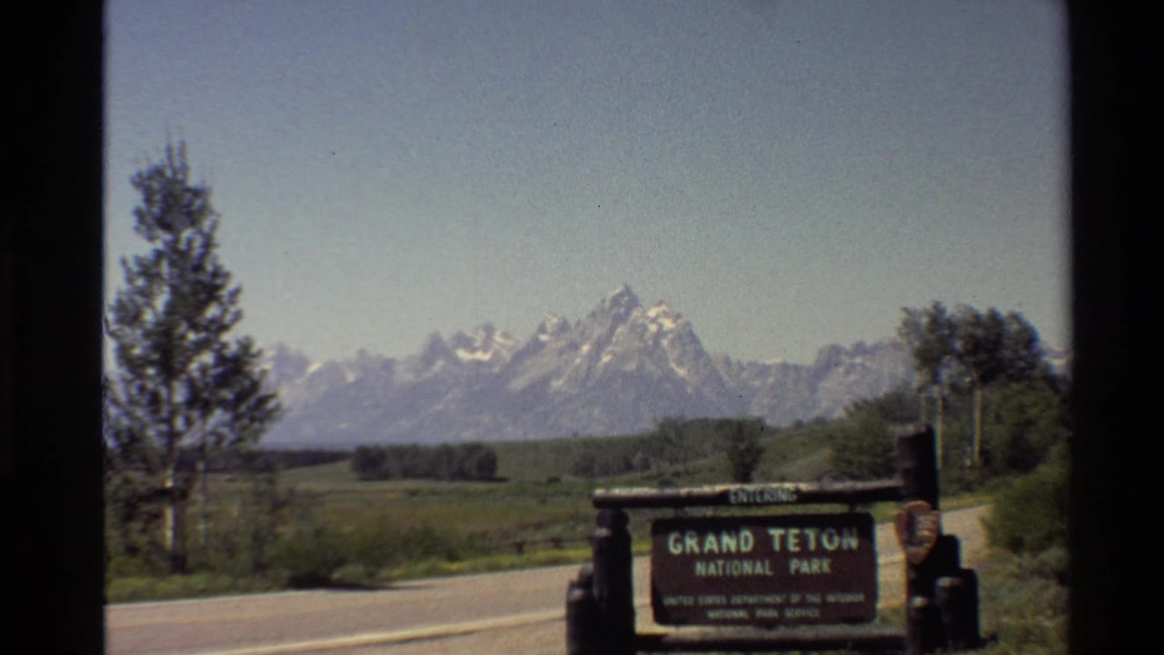 Grand Teton National Park sign and mountain range framed from a moving roadside view.