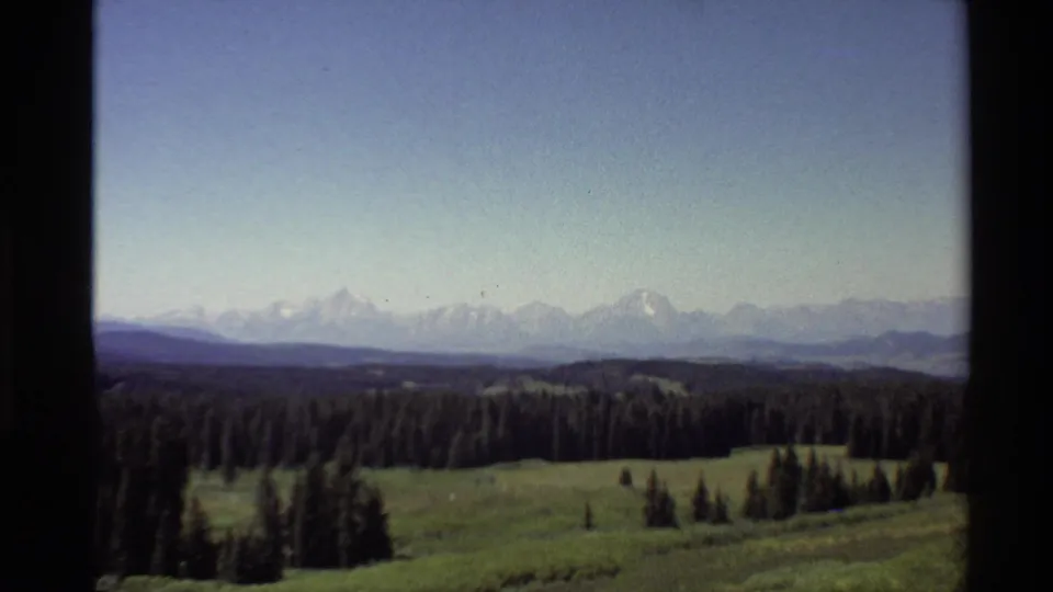 By the final frame, daylight shows a broad Western U.S. forest and meadow view with snow-capped peaks in the distance.