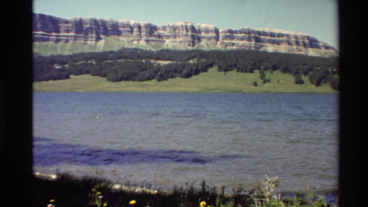 Wide river view with a distant tree line and banded rock formation across the water.