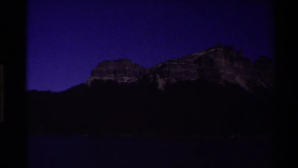 Twilight 8mm frame from the 1980 Western USA footage showing a mountain and shoreline darkened against a deep purple sky.