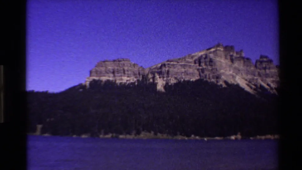 1980 Western USA 8mm frame showing a mountain ridge, forested shore, lake surface, and vivid purple evening sky.