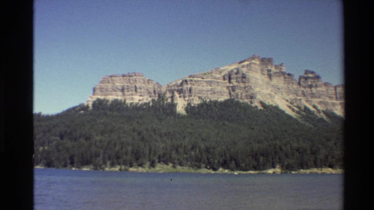Distant layered mountain range above evergreen forest and blue water.