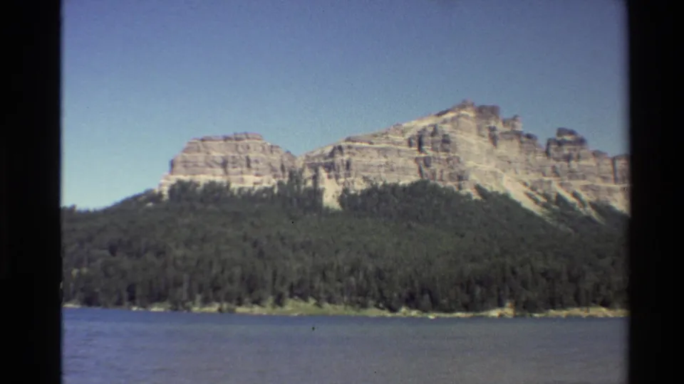 1980 8mm Western U.S. home-movie view of pale layered mountains rising beyond forest and a lake or river.