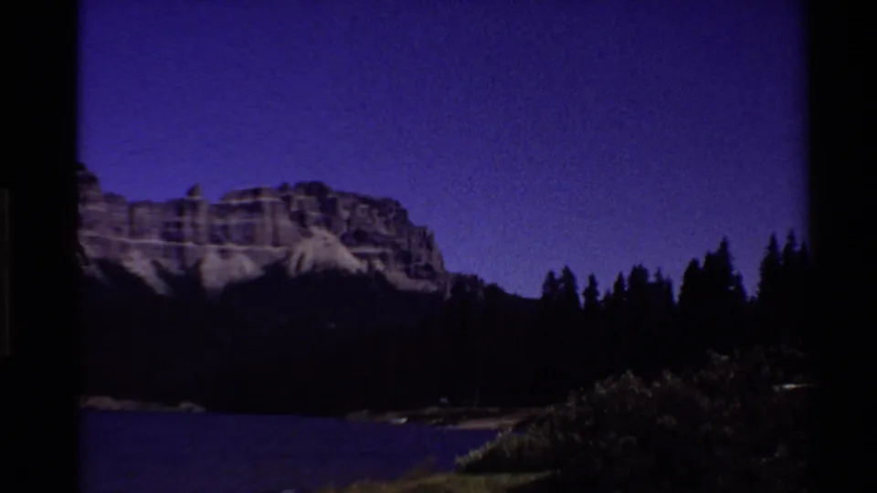 Dusk view of the Western U.S. mountain lake landscape with pine silhouettes and a deep purple sky on 8mm film.