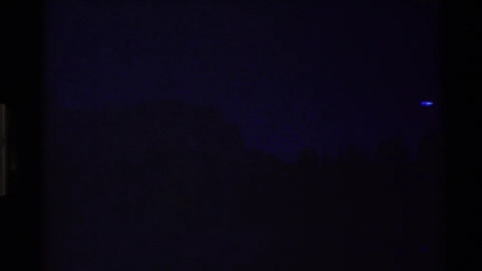 Underexposed transition frame from the 8mm reel, with mostly dark image area and faint blue light near the center.