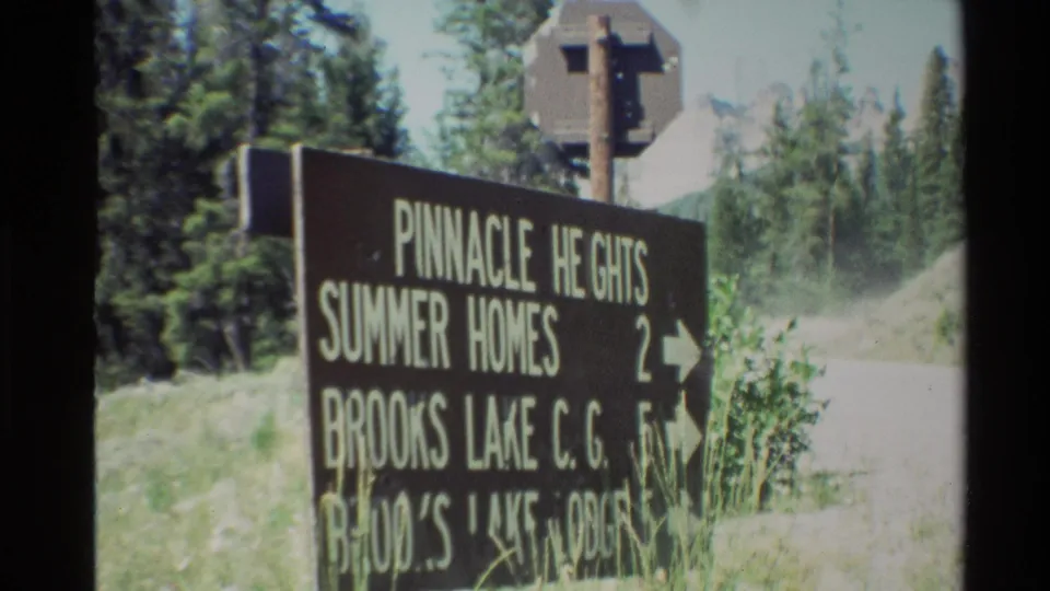 Final 8mm frame of the roadside sign, with Pinnacle Heights Summer Homes and Brooks Lake destination text visible against trees and a bright road.