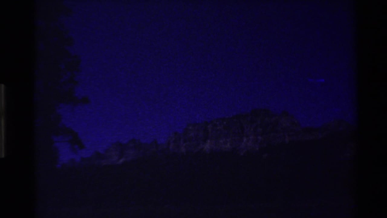 Blue-tinted 8mm view of a distant mountain ridge and dark tree shapes, consistent with the clip's Western USA mountain setting.