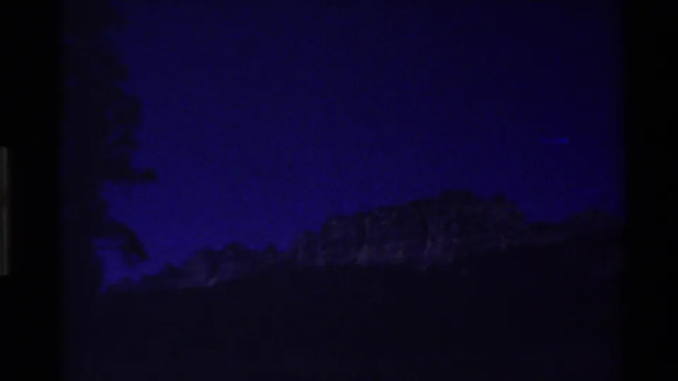Blue-tinted 8mm view of a distant mountain ridge and dark tree shapes, consistent with the clip's Western USA mountain setting.