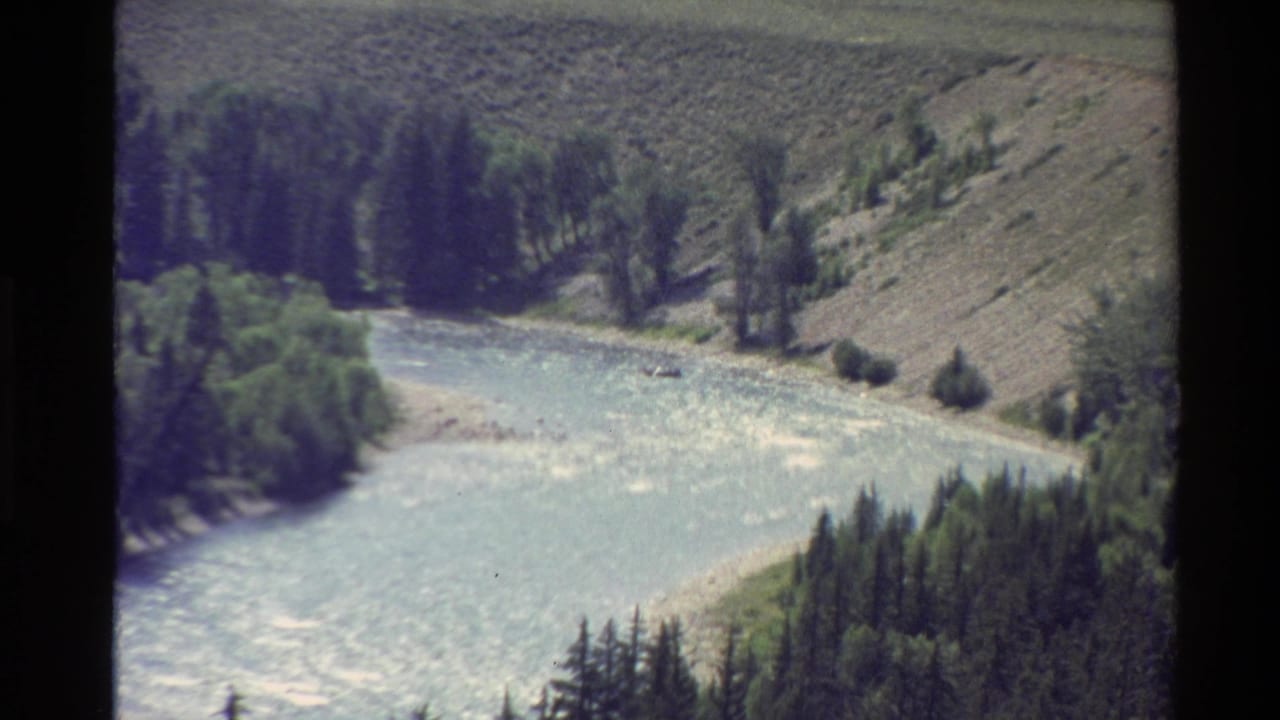 River bend with rippled water, evergreen stands, rocky banks, and dry hillside slopes.