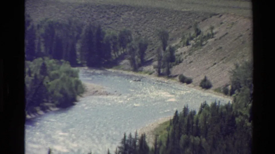 Western U.S. 8mm frame of a fast river moving through a green and scrub-covered mountain valley.