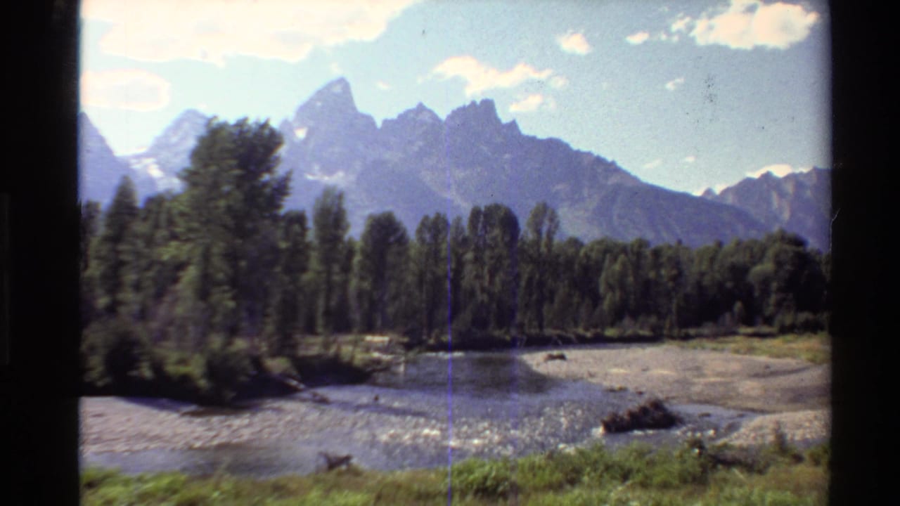 1980 Western U.S. home-movie view of a river flowing below tree-covered banks and jagged mountains.