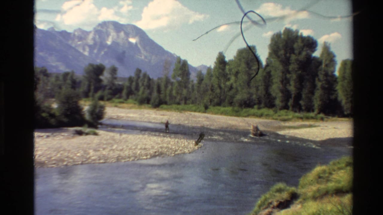 River and gravel bar with a distant fisher, trees, mountains, and film scratches.