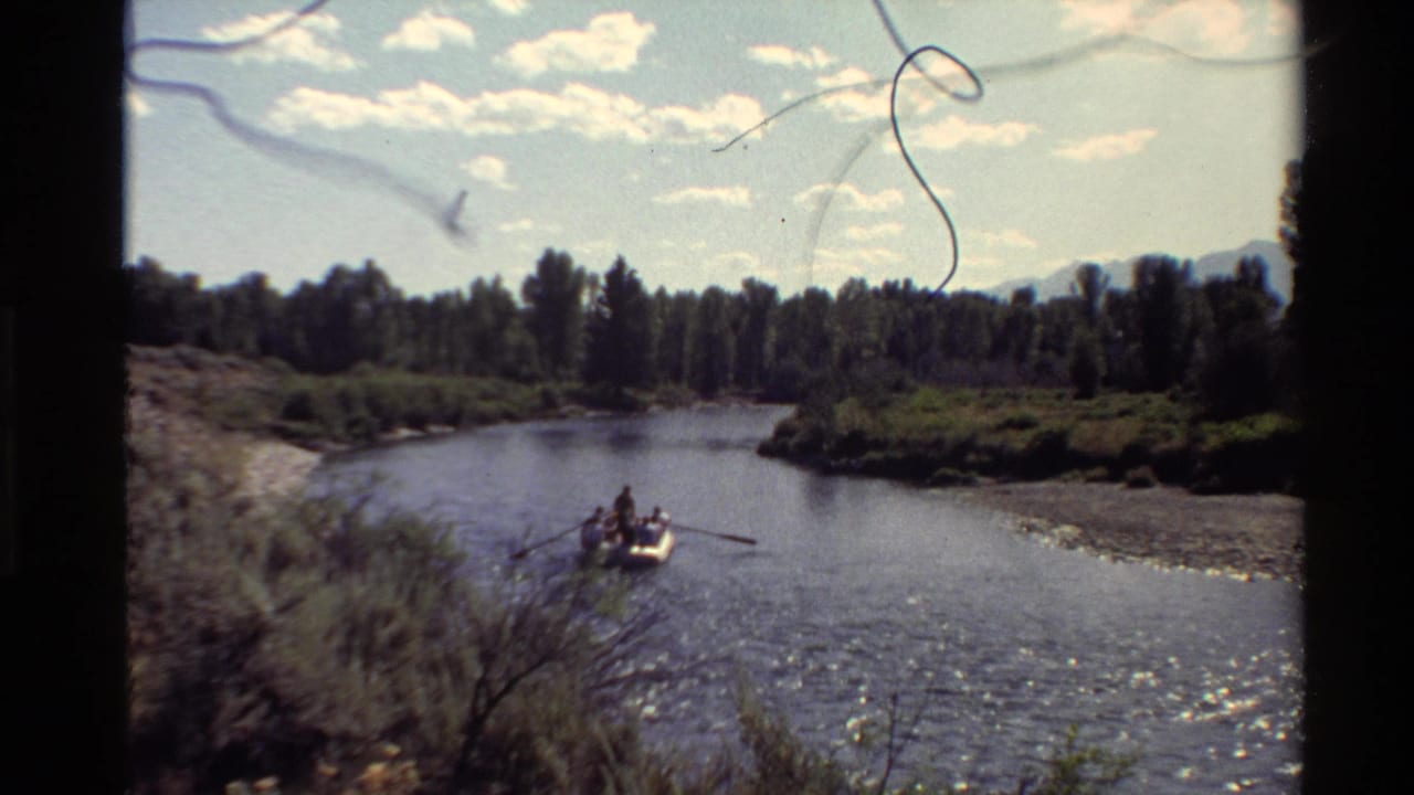 1980 Western USA 8mm frame showing a small rowboat on a calm river below a bright clouded sky and tree-lined banks.