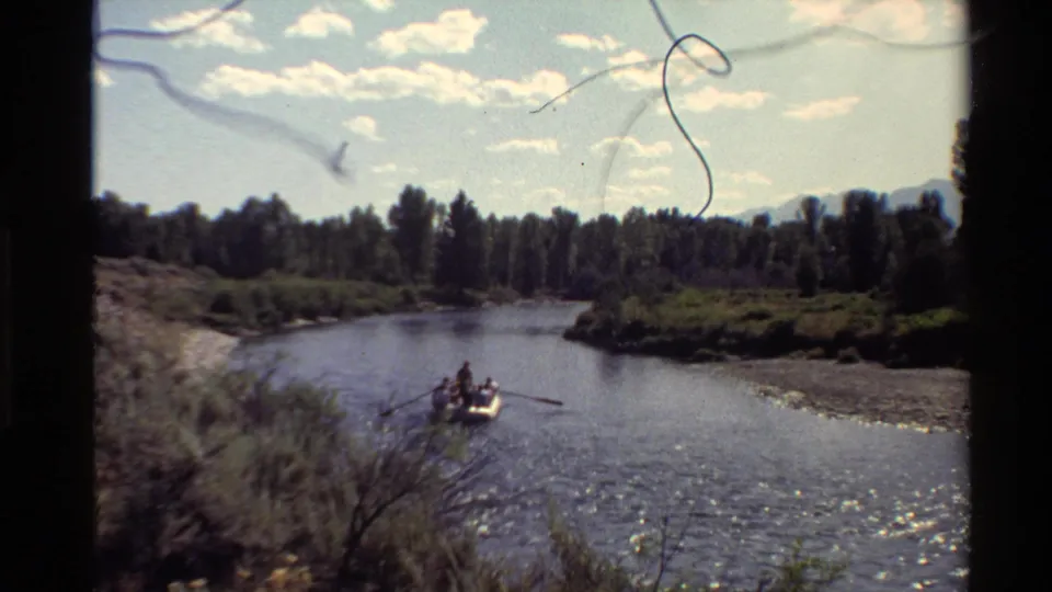1980 Western USA 8mm frame showing a small rowboat on a calm river below a bright clouded sky and tree-lined banks.