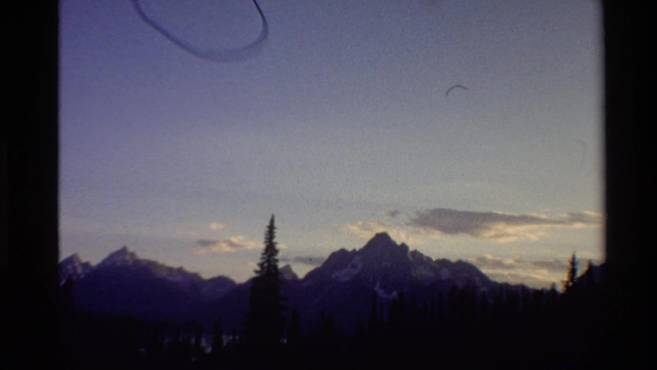 1980 Western U.S. 8mm frame showing distant mountain peaks, tree silhouettes, pale dusk sky, and visible film border artifacts.
